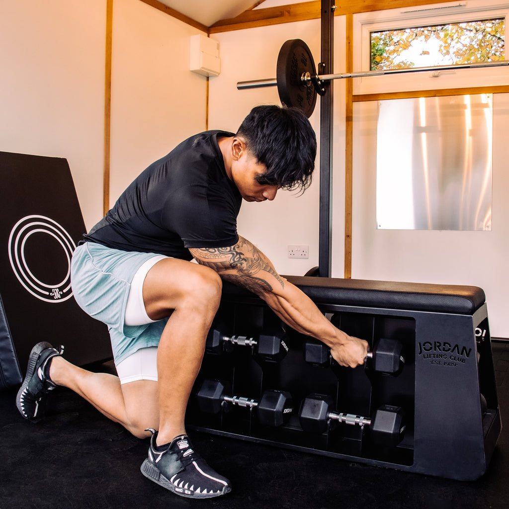 Man next to Jordan Lifting Club Flat HIIT Bench. Picking up a hex dumbbell